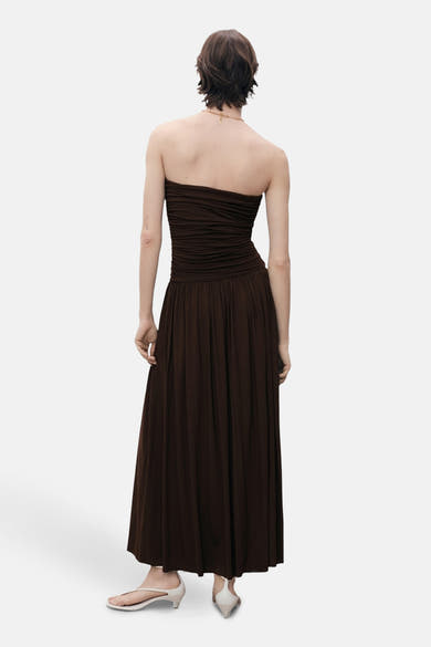 Robe longue marron de MANGO, coupe bustier et plissée, portée avec des sandales à talons ouverts.