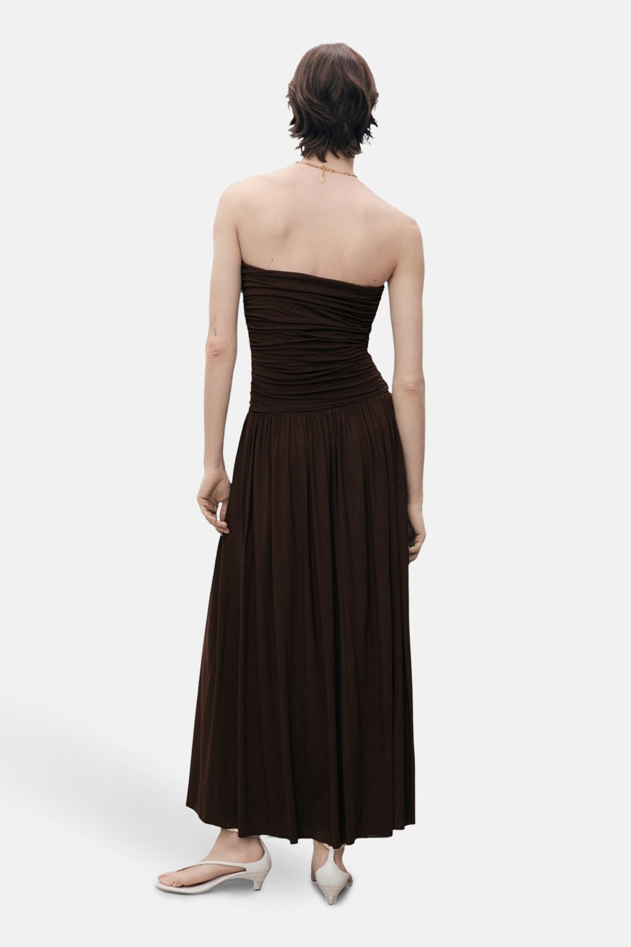 Robe longue marron de MANGO, coupe bustier et plissée, portée avec des sandales à talons ouverts.
