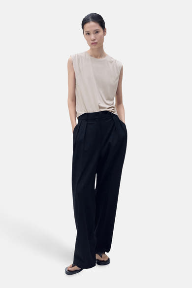 Beige mouwloze top van MANGO, gedragen met een wijde zwarte broek en sandalen.