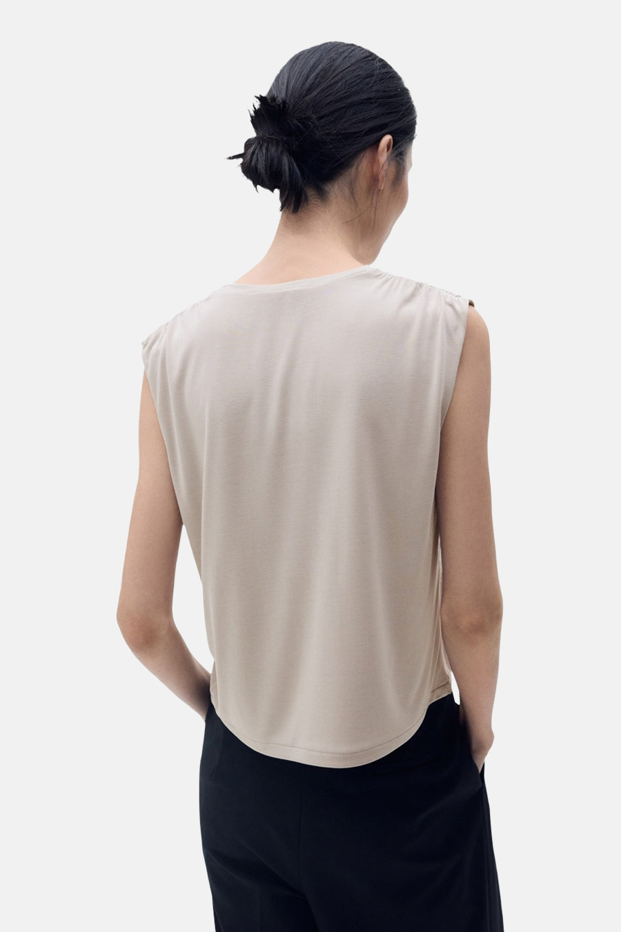 Top sans manches beige de MANGO, présentant un dos uni et porté avec un pantalon noir.
