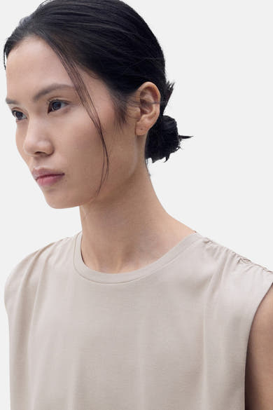 Beige mouwloze top van MANGO, gedragen door een model, met geplooide details op de schouder.