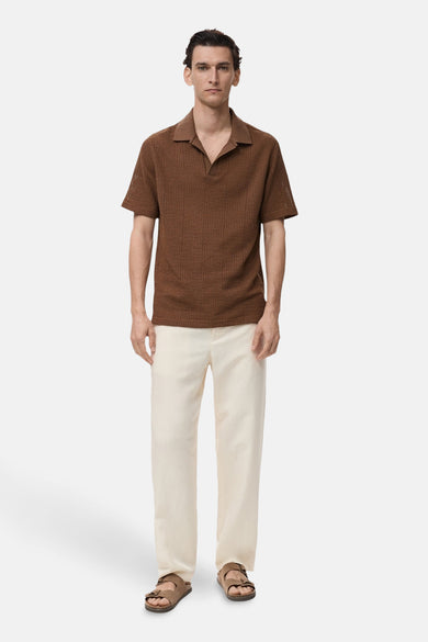 Bruin poloshirt met korte mouwen van MANGO, in textuurgebreid materiaal, gedragen met een witte broek en sandalen.