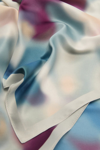 Foulard bleu, de MANGO, avec un motif abstrait multicolore et une bordure unie.