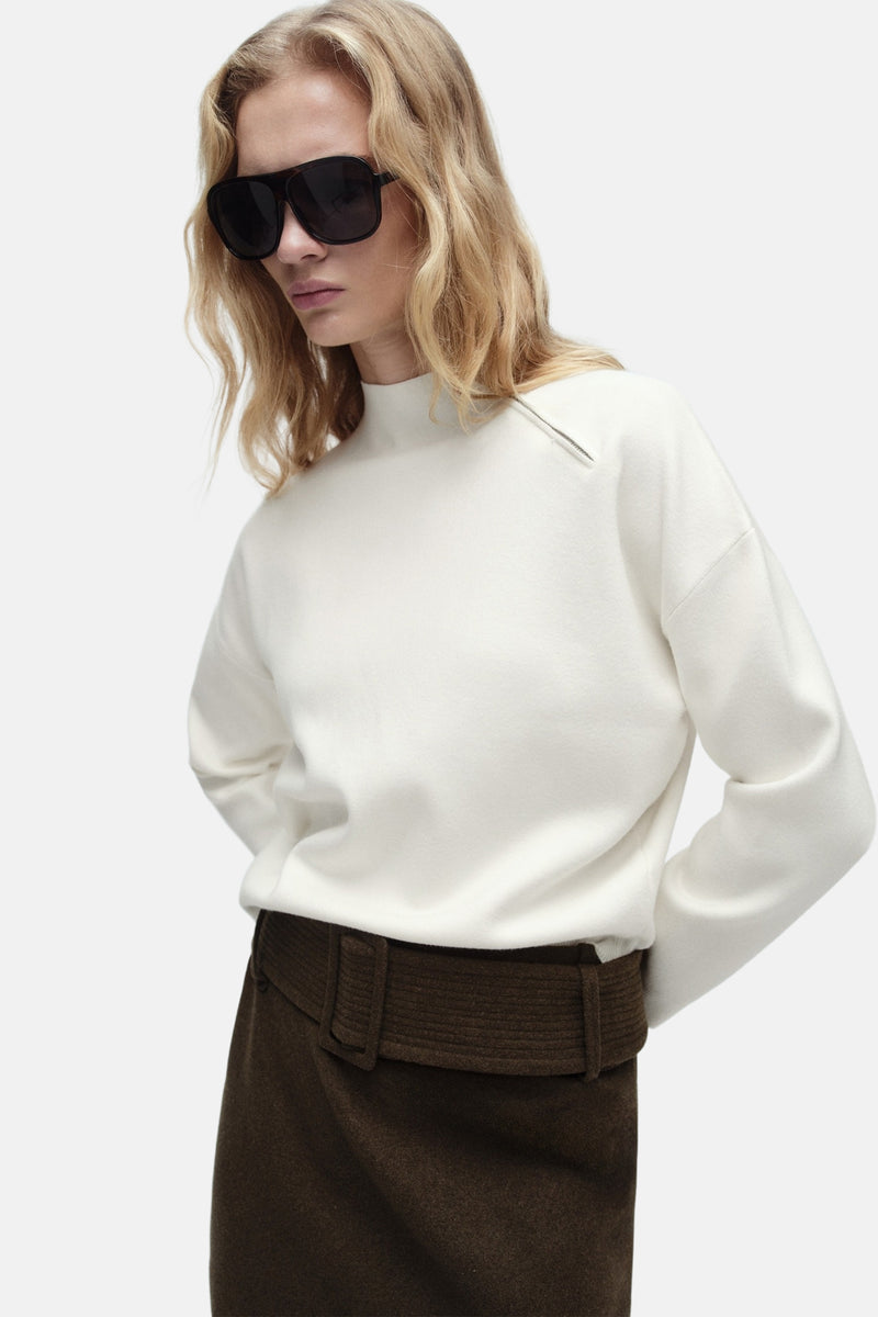 Witte ronde nekpullover van MANGO, met een decoratieve knoop aan de schouder en gedragen met eenbrubruine rok.