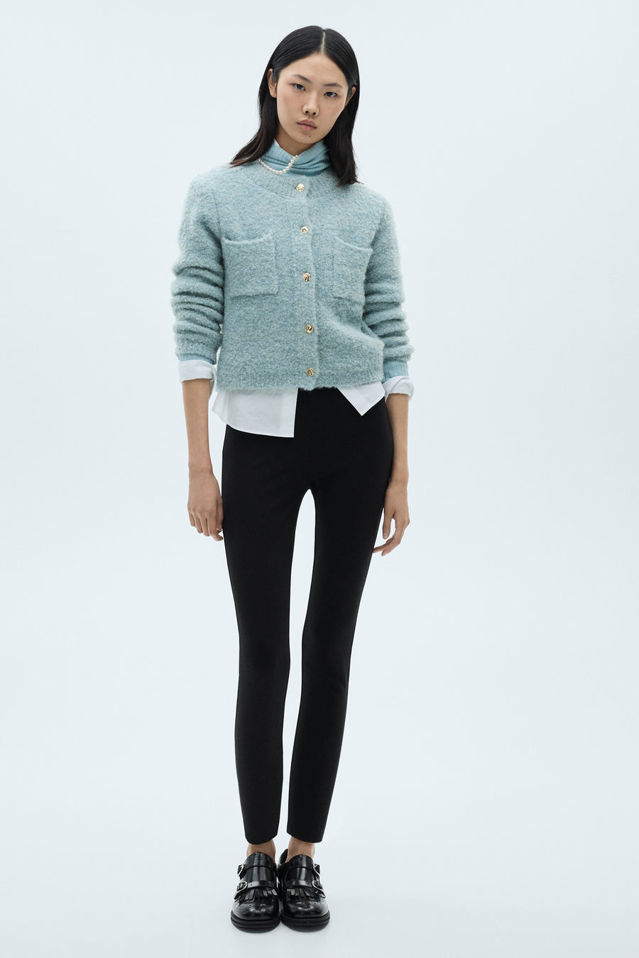 Blauwe MANGO bodywarmer met gouden knopenzakken gedragen over een witte blouse en een zwarte broek.