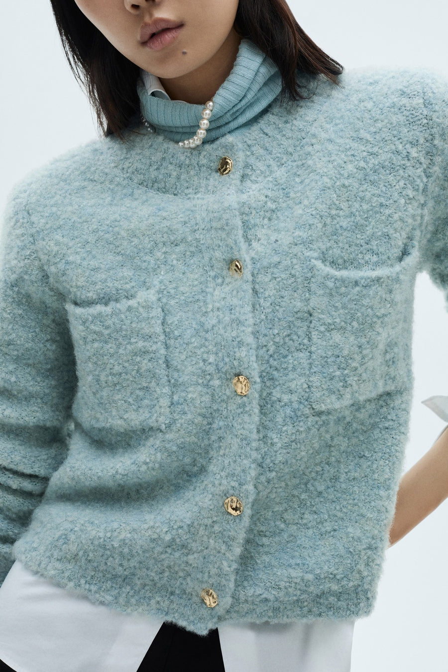 Blauwe MANGO bodywarmer met gouden knopen, opgestikte zakken en een bouclétextuur, gedragen over een coltrui.