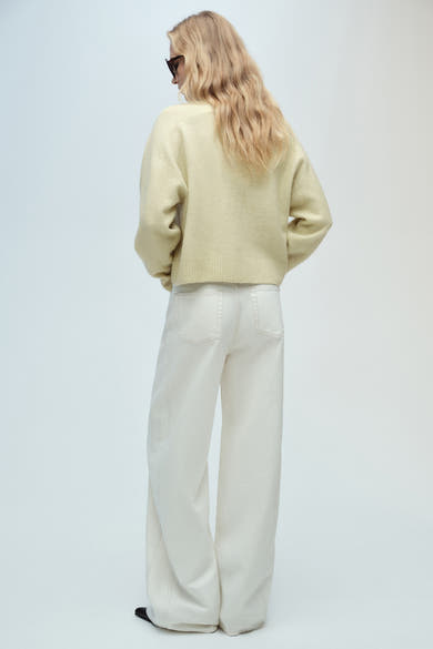 Pull à col en V vert de MANGO, porté avec un jean blanc à jambes larges, vue de dos.