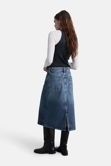 Midi-rok van middinblauw denim van MANGO, met split aan de achterkant en gedragen met zwarte laarzen.