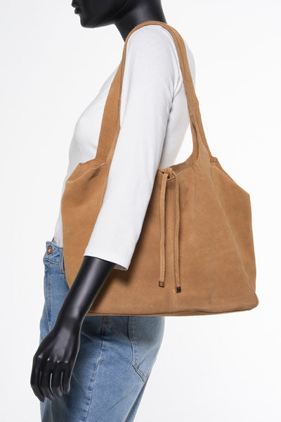 Bruine suède handtas van MANGO, gedragen over de schouder door een model, met blauwe jeans en witte top.