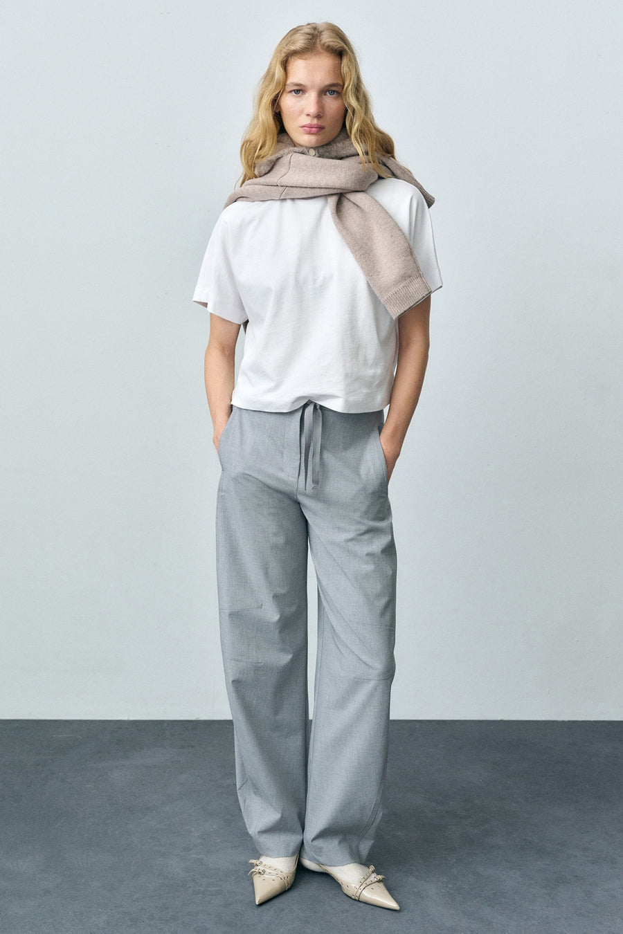 Wit T-shirt met korte mouwen van MANGO, gedragen met een grijze broek en een beige sjaal.