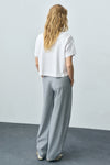 Wit T-shirt met korte mouwen van MANGO, gedragen met een grijze broek met hoge taille en sandalen.