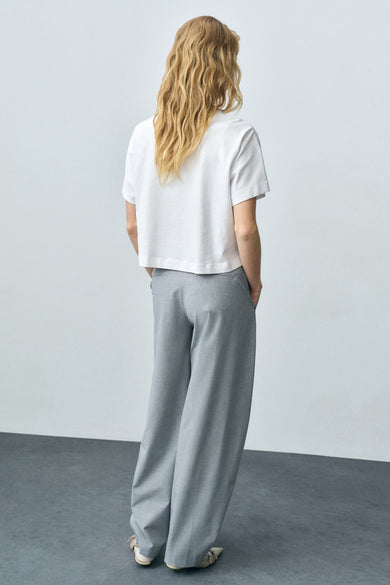 T-shirt blanc à manches courtes de MANGO, porté avec un pantalon gris taille haute et des sandales.