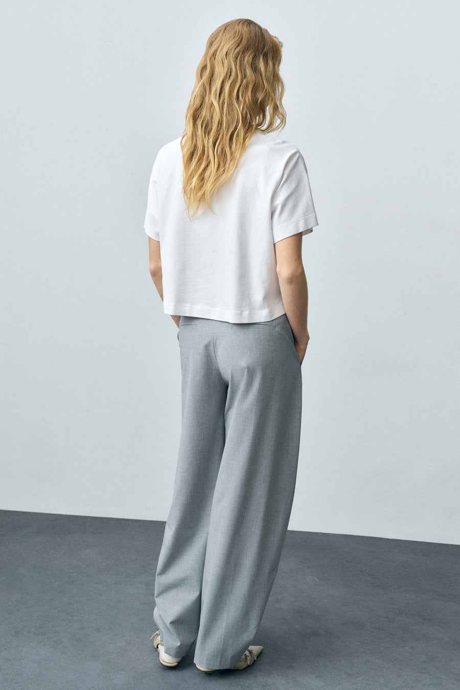 Wit T-shirt met korte mouwen van MANGO, gedragen met een grijze broek met hoge taille en sandalen.