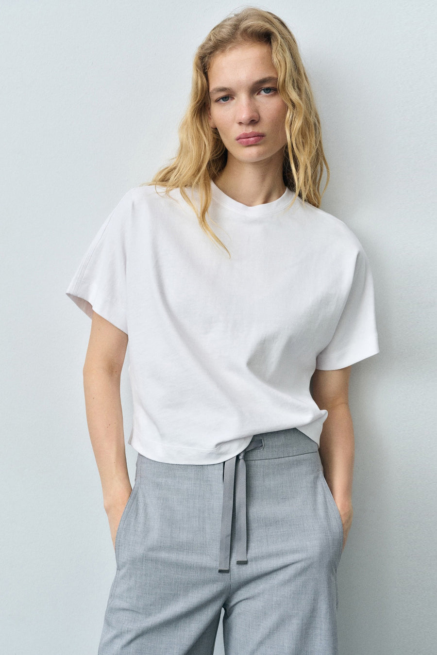Wit T-shirt met korte mouwen van MANGO, gedragen met een grijze broek met trekkoord.