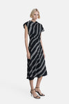 Zwarte gestreepte jurk van MANGO, asymmetrische midi-snit met witte strepen, gedragen met zwarte sandalen met bandjes.