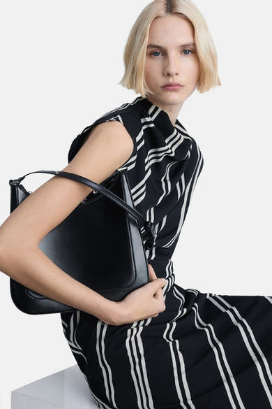 Zwarte gestreepte jurk van MANGO, gedragen door een blondine met een zwarte tas.