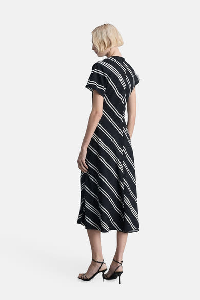 Robe noire à rayures, par MANGO, avec des détails de style et chaussures à talons noirs.
