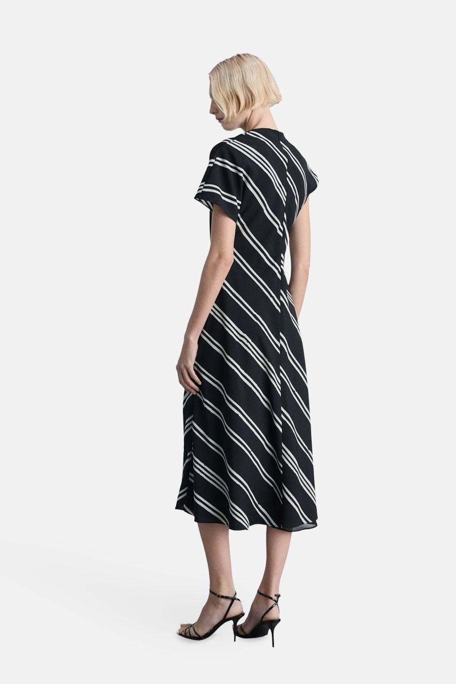 Robe noire à rayures, par MANGO, avec des détails de style et chaussures à talons noirs.
