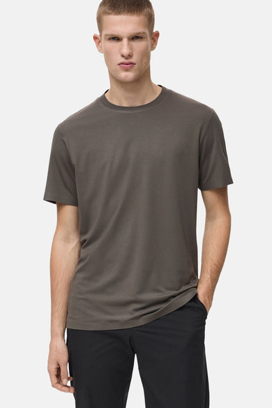 T-shirt kaki à manches courtes de MANGO, porté avec un pantalon noir, une main dans la poche.