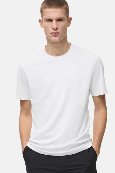 T-shirt blanc à manches courtes de MANGO, porté avec un pantalon noir et les mains dans les poches.