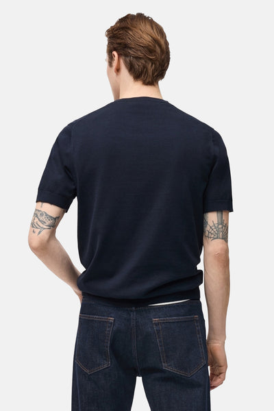 T-shirt à manches courtes bleu foncé de MANGO, porté avec un jean, vue de dos et tatouages visibles sur les bras.