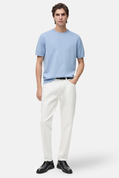 T-shirt bleu clair à manches courtes de MANGO, porté avec un pantalon blanc et des chaussures noires.
