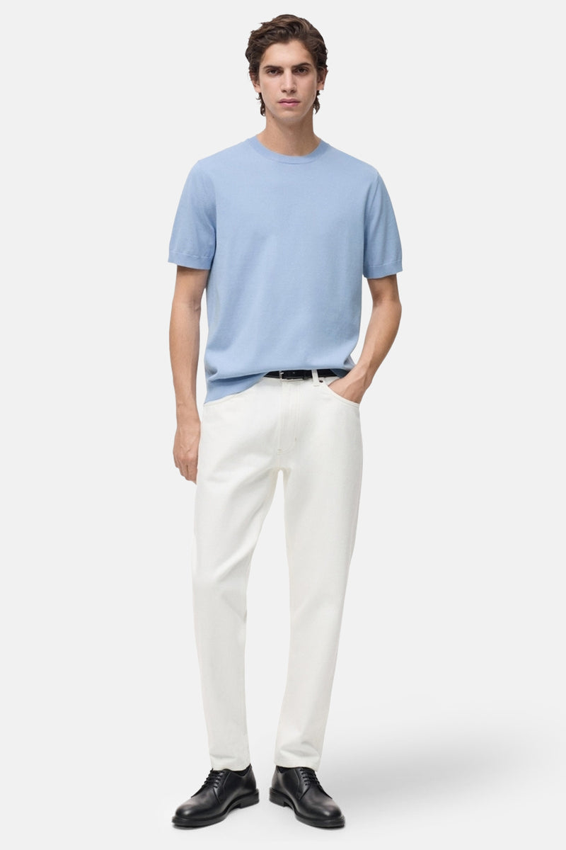 T-shirt bleu clair à manches courtes de MANGO, porté avec un pantalon blanc et des chaussures noires.
