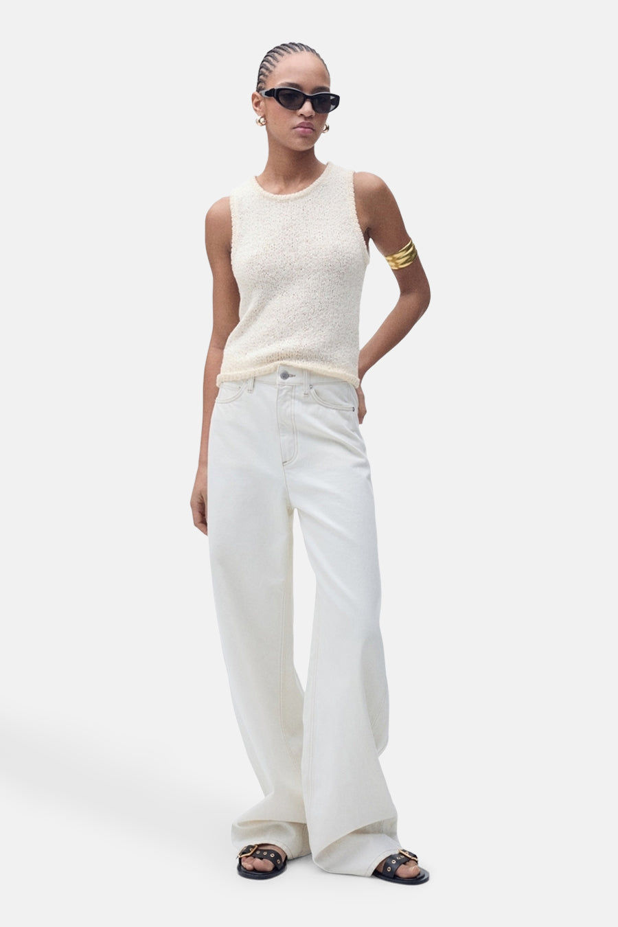 Top écru sans manches de MANGO, porté avec un pantalon blanc ample et des sandales noires.
