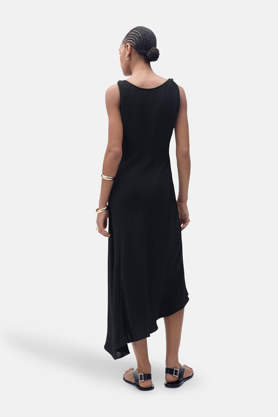 Robe noire asymétrique de MANGO, avec des détails de texture subtils et des sandales noires minimalistes.