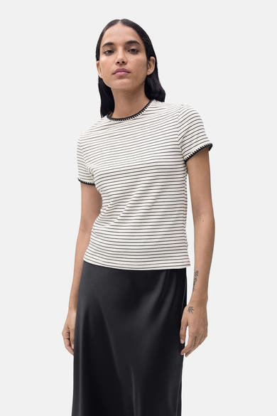 T-shirt à manches courtes beige de MANGO, rayures noires horizontales et finitions noires, porté avec une jupe noire.
