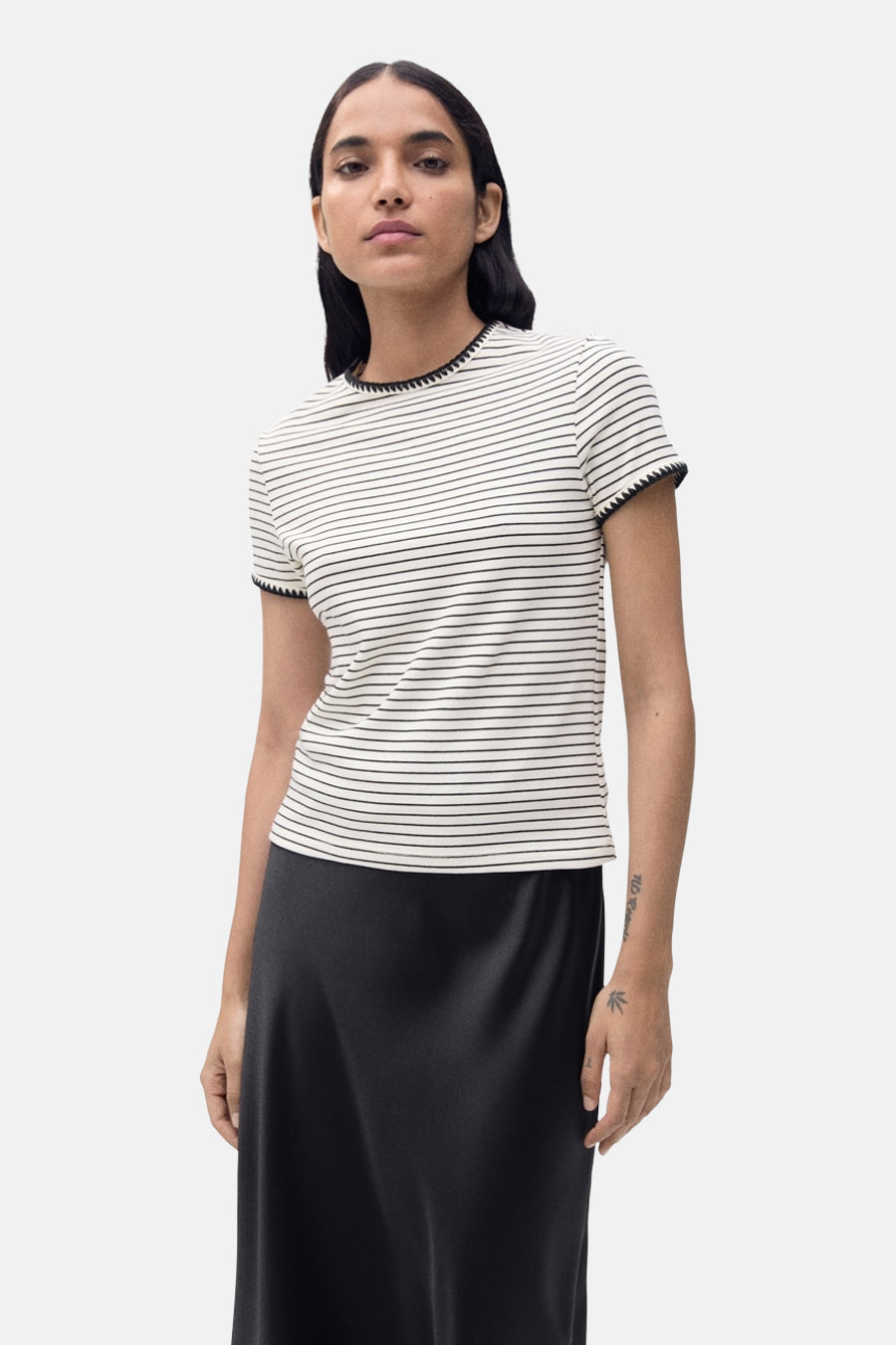 T-shirt à manches courtes beige de MANGO, rayures noires horizontales et finitions noires, porté avec une jupe noire.
