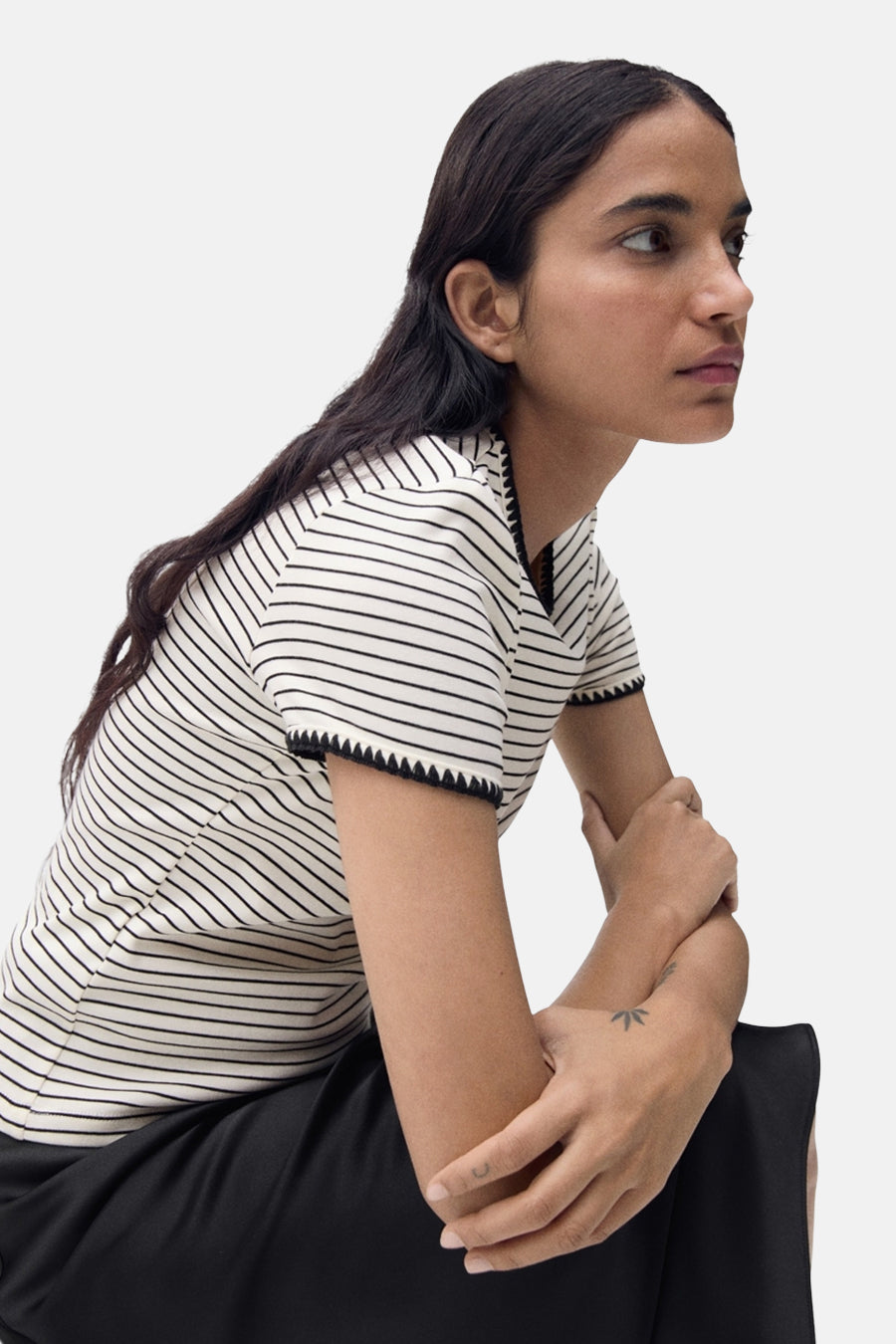 T-shirt beige à rayures by MANGO, avec finitions festonnées aux manches, porté avec une jupe noire.
