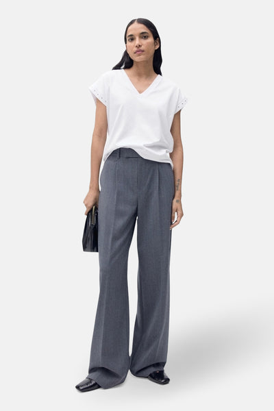 T-shirt blanc à manches courtes de MANGO, porté avec un pantalon gris à plis et chaussures noires.