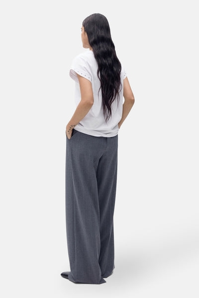 T-shirt blanc à manches courtes de MANGO, avec des détails de clous sur les épaules, porté avec un pantalon large.