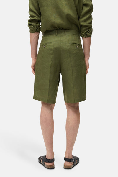 Short vert en lin de MANGO, avec poches boutonnées à l'arrière, porté avec des sandales à lanières.

