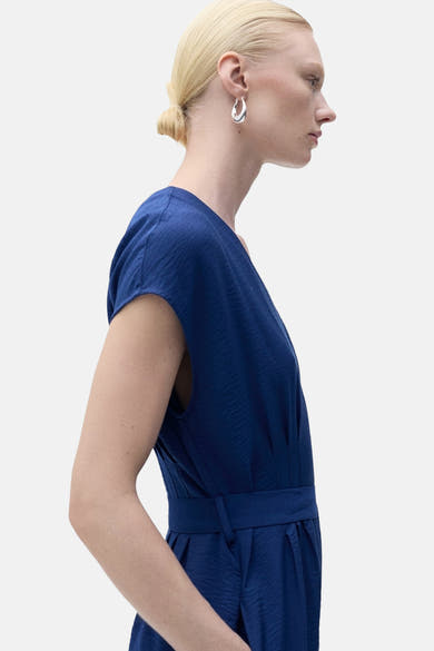 Blauwe jumpsuit van MANGO, met een gekreukte textuur en een bijpassende ceintuur in de taille, van opzij gezien.