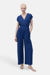 Blauwe jumpsuit van MANGO, met strikceintuur en wijde pijpen, gedragen met witte hakken.