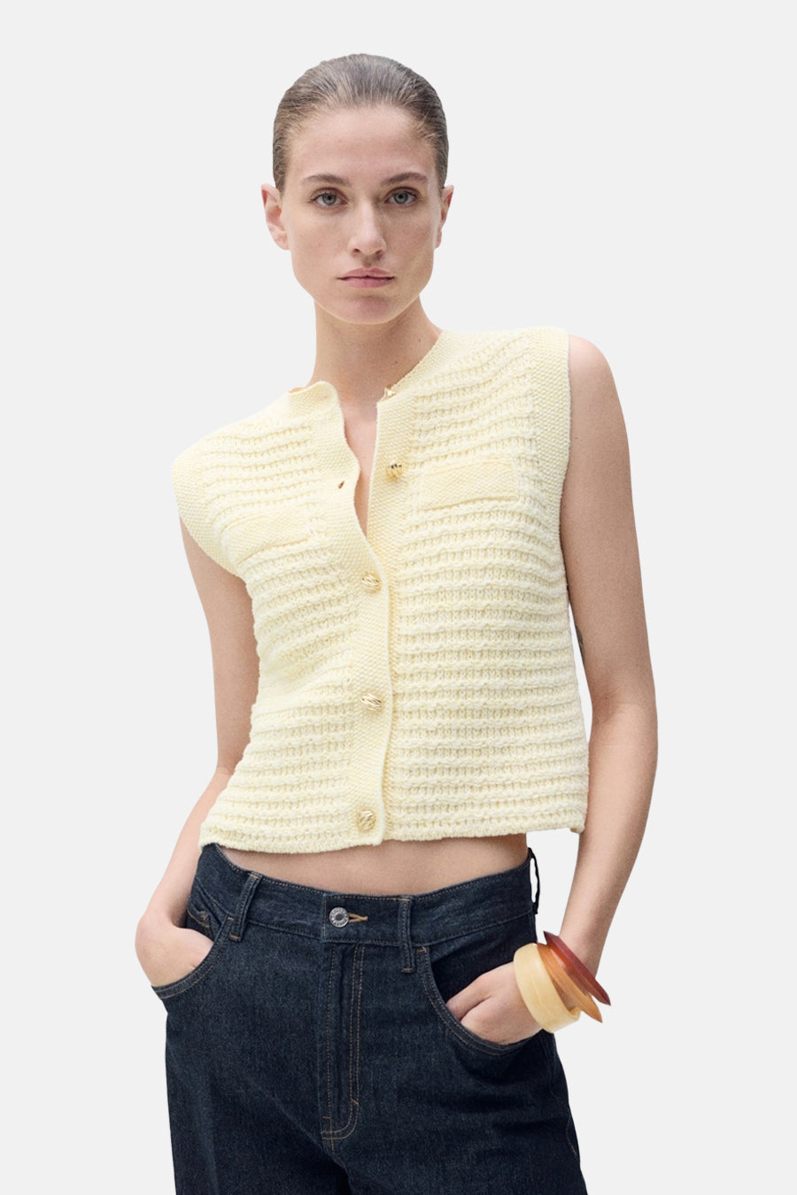Gilet jaune en tricot de MANGO, boutonné et porté avec un jean taille basse.
