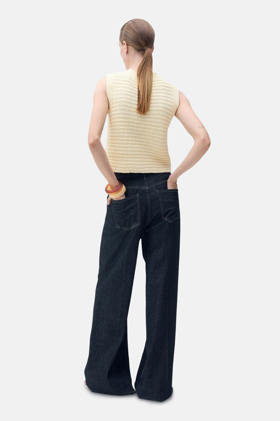 Gilet jaune de MANGO, en maille ajourée, porté avec un pantalon évasé en denim.