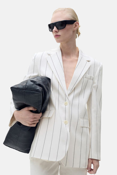 Witte MANGO blazer met strepen, gedragen met een zwarte zonnebril en een zwarte gewatteerde tas.
