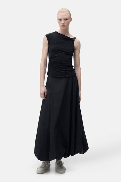 Zwarte mouwloze top van MANGO, met een metalen sluiting op één schouder, gedragen met een lange zwarte rok en sneakers.