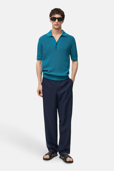 Turquoise poloshirt met korte mouwen van MANGO, in geribbelde stof gedragen met een marineblauwe broek en zwarte sandalen.