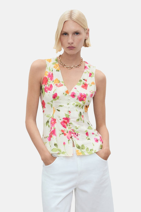 Multikleurig mouwloos bloesje van MANGO, met bloemenprint, met een strikkoord aan de achterkant en gedragen met een witte korte broek.