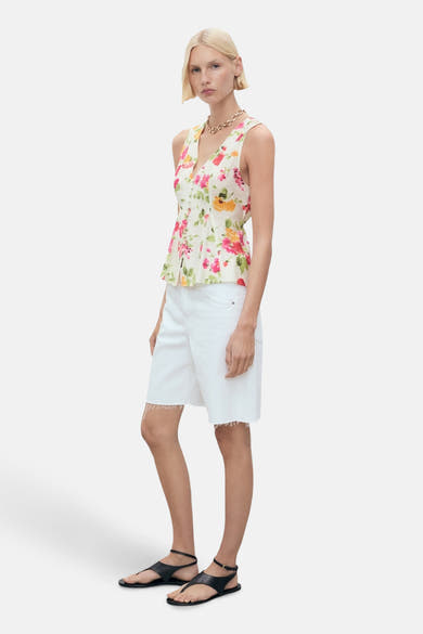 Blouse sans manches multicolore de MANGO, à motif fleuri, portée avec un short blanc et des sandales noires.

