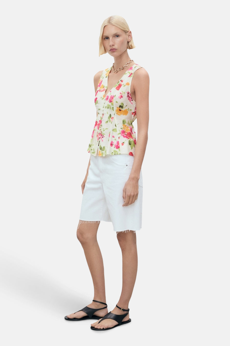 Blouse sans manches multicolore de MANGO, à motif fleuri, portée avec un short blanc et des sandales noires.
