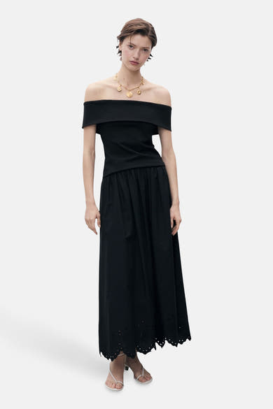 Zwarte lange rok van MANGO, met broderiedetail aan de zoom, gedragen met een zwarte top en een gouden ketting.