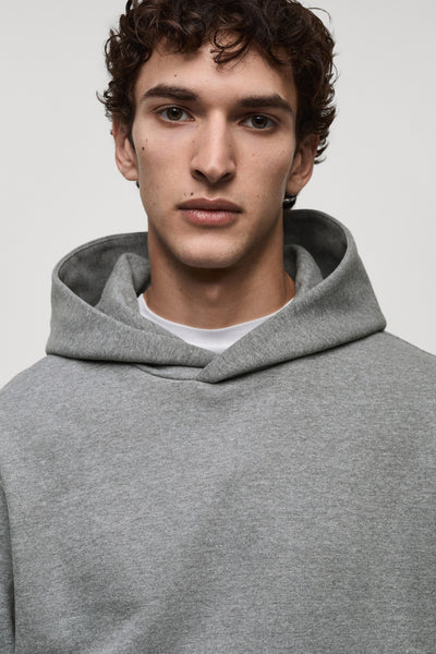 Gemêleerd grijze hoodie van MANGO, gedragen door een man, met een wit T-shirt zichtbaar bij de kraag.