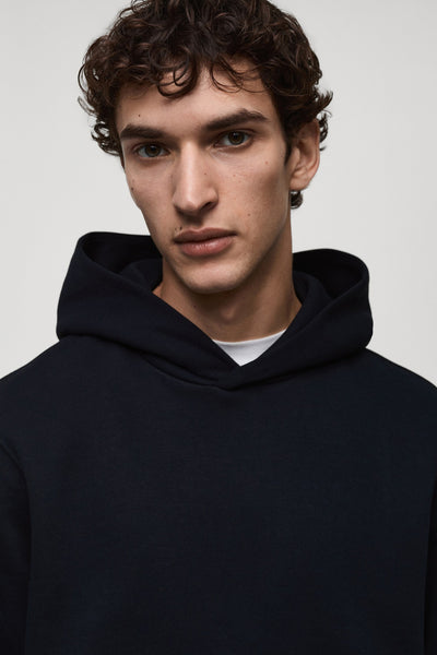 Blauwe hoodie van MANGO, met wijde capuchon en trekkoorden, gedragen over een wit T-shirt.