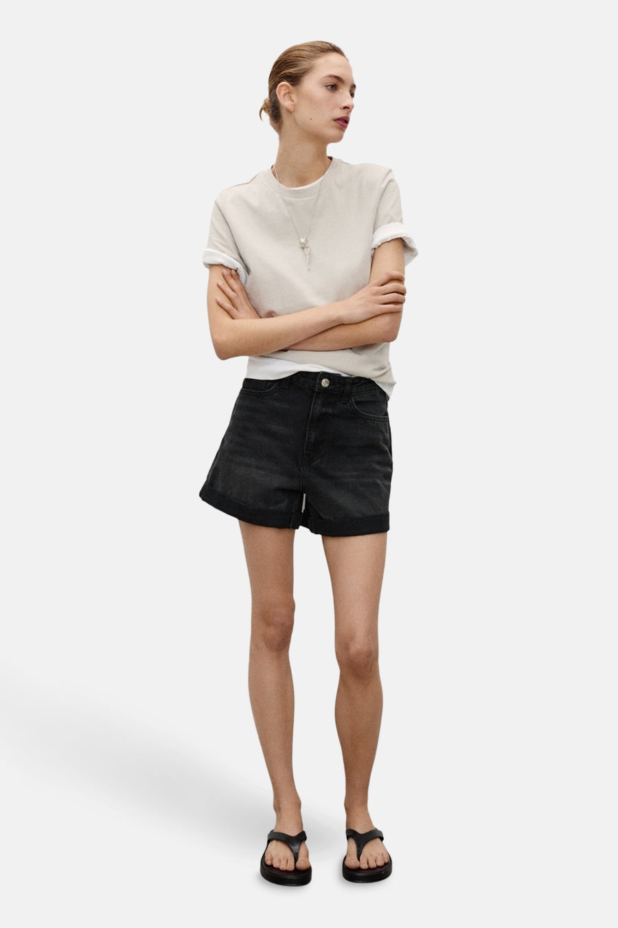 Korte zwarte spijkerbroek van MANGO, gedragen met een crèmekleurig T-shirt en zwarte sandalen.
