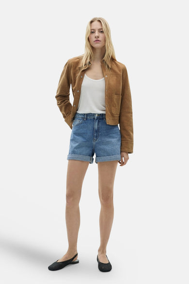 Short en denim bleu moyen de MANGO, porté avec un débardeur blanc et une veste marron.